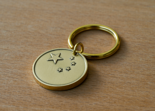Gold metallic keychain with a circular tag engraved with five stars, resting on a wooden surface