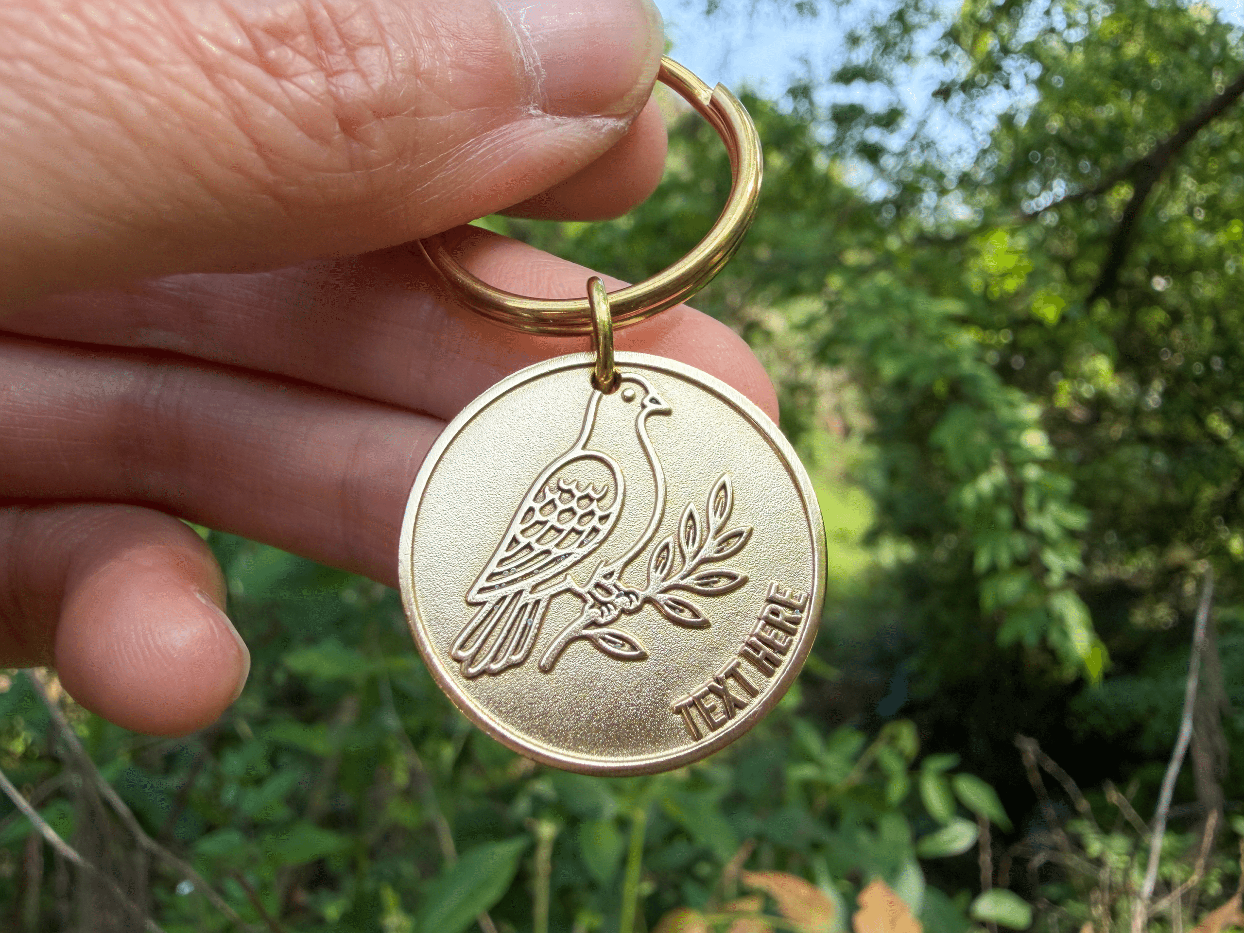 Circular brass tag engraved with a dove on a branch and customizable text reading TEXT HERE