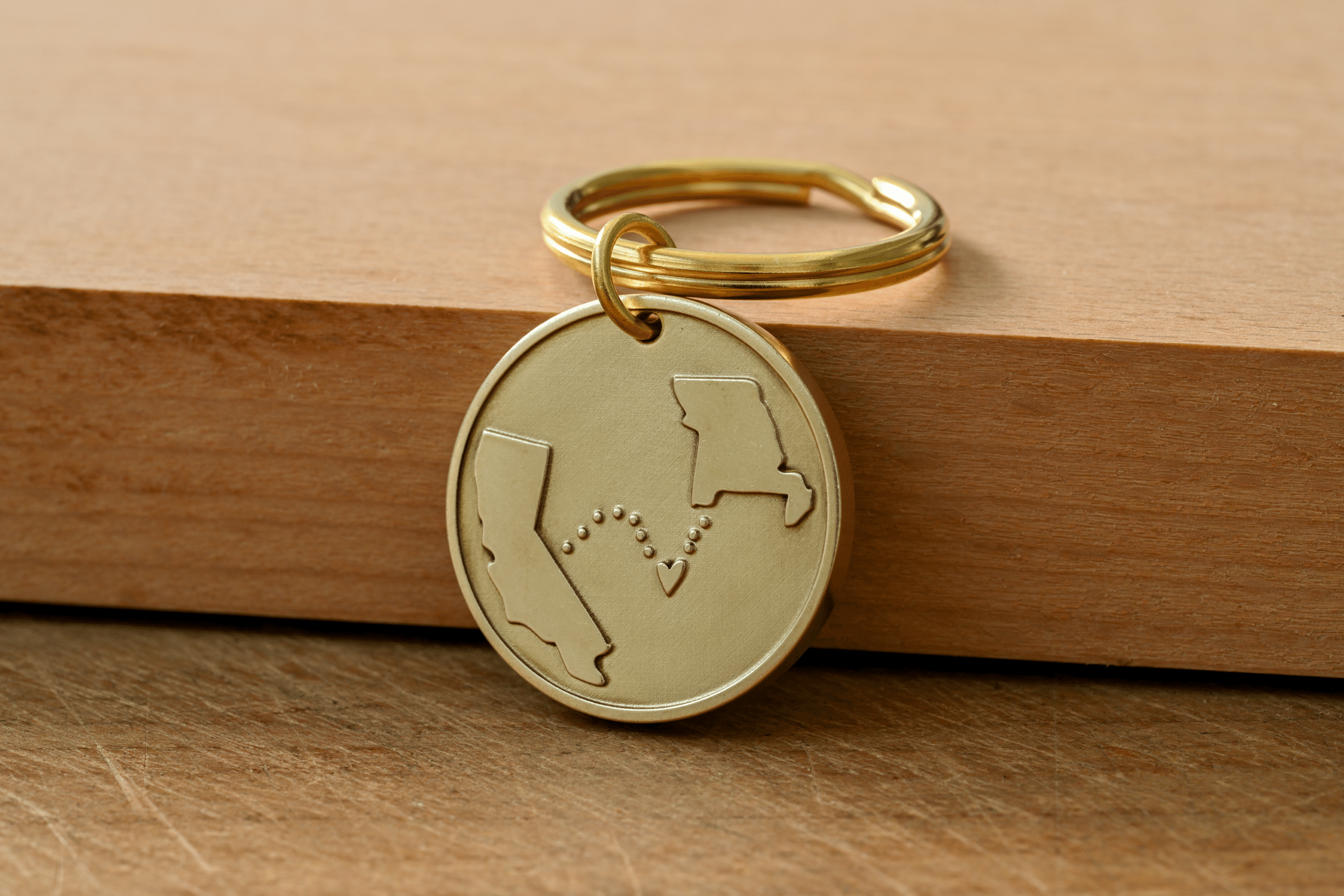 Brass keychain engraved with outlines of California and Missouri connected by a dotted line with a small heart