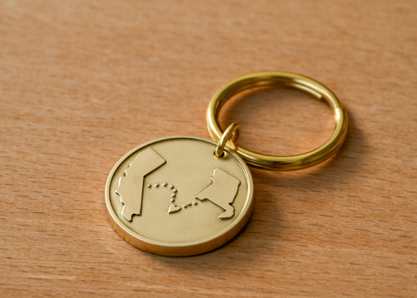 Gold circular keychain engraved with outlines of California and Louisiana connected by a dotted line with a heart