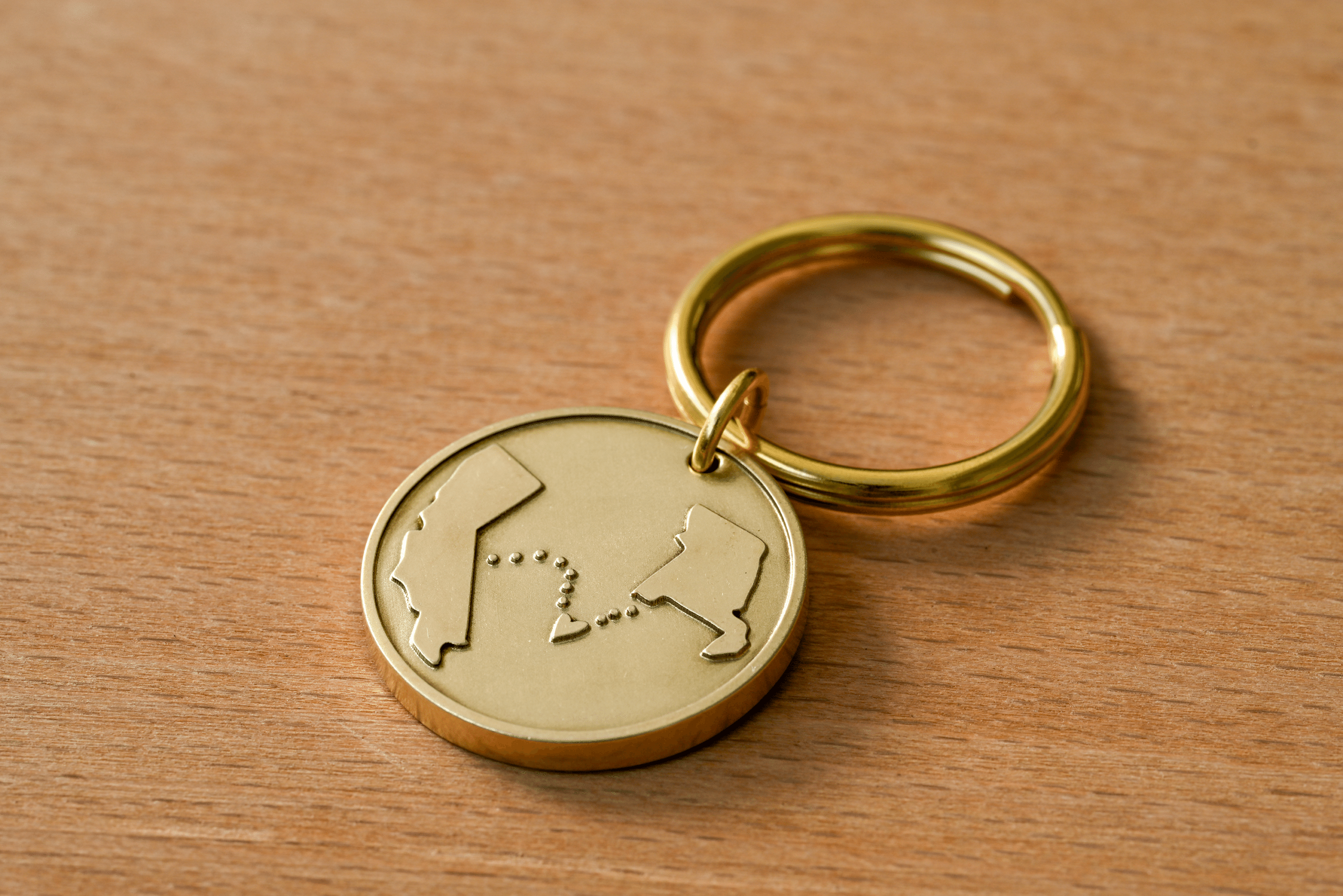 Gold circular keychain engraved with outlines of California and Louisiana connected by a dotted line with a heart