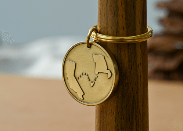 Round brass keychain engraved with California and Missouri connected by a dotted path with a heart