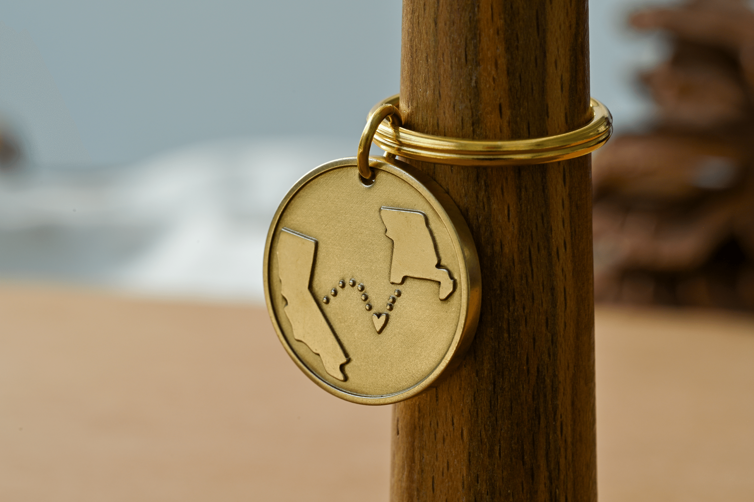 Round brass keychain engraved with California and Missouri connected by a dotted path with a heart