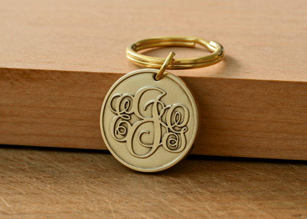 Round brass keychain tag with an engraved ornate monogram on a key ring resting on a wooden surface