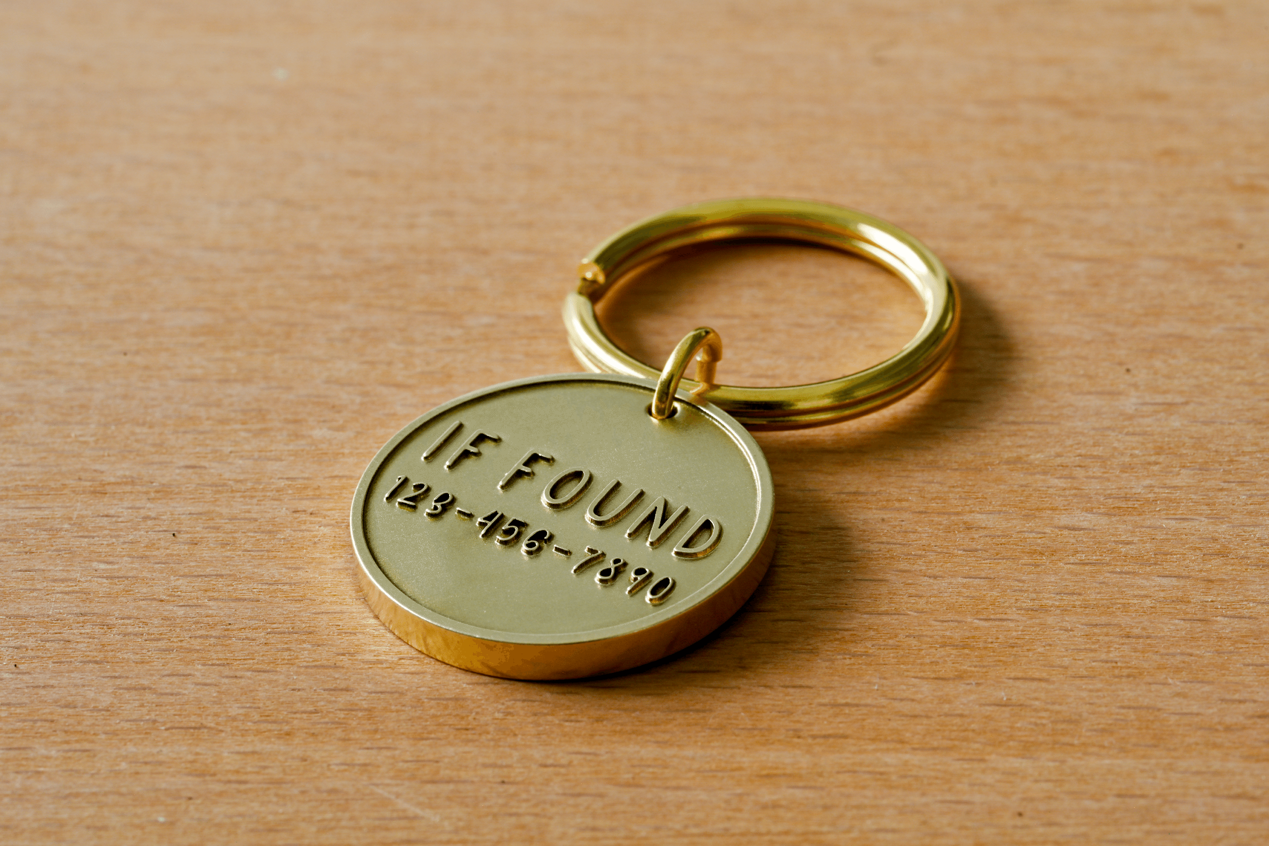 Round brass key tag attached to a keyring, engraved with IF FOUND 123-456-7890