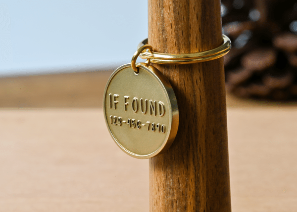 Round brass tag on a key ring engraved with IF FOUND 123-456-7890