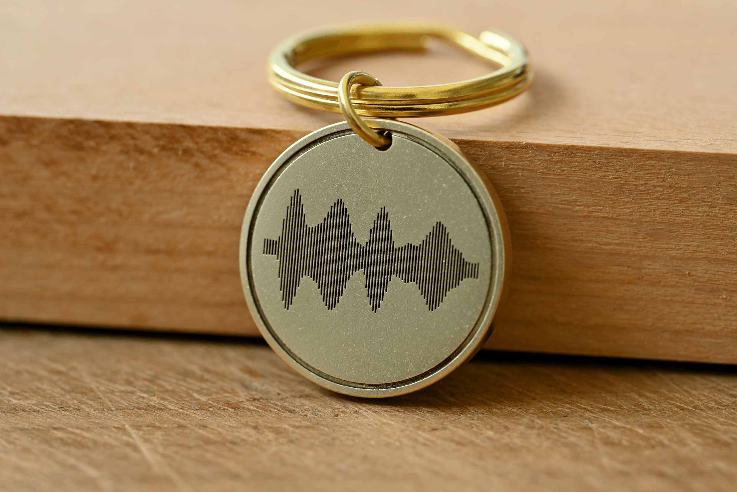 Round brass keychain tag engraved with an audio soundwave design