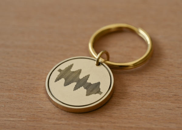Gold circular keychain engraved with a sound wave pattern on a wooden background