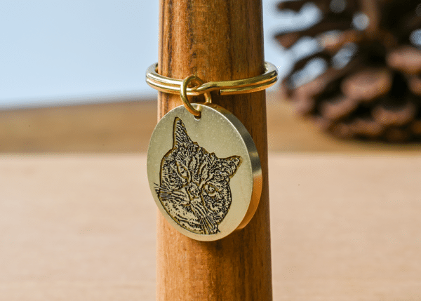 Round gold keychain tag engraved with a detailed portrait of a cat's face
