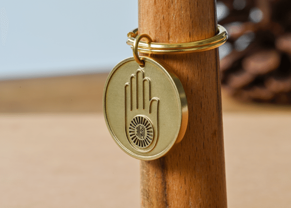 Brass keychain featuring a circular medallion embossed with the Jain Ahimsa hand symbol