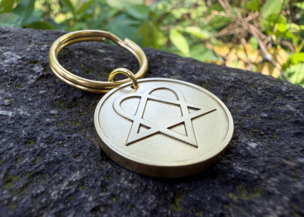 Brass keychain with an engraved heartagram symbol resting on a stone surface