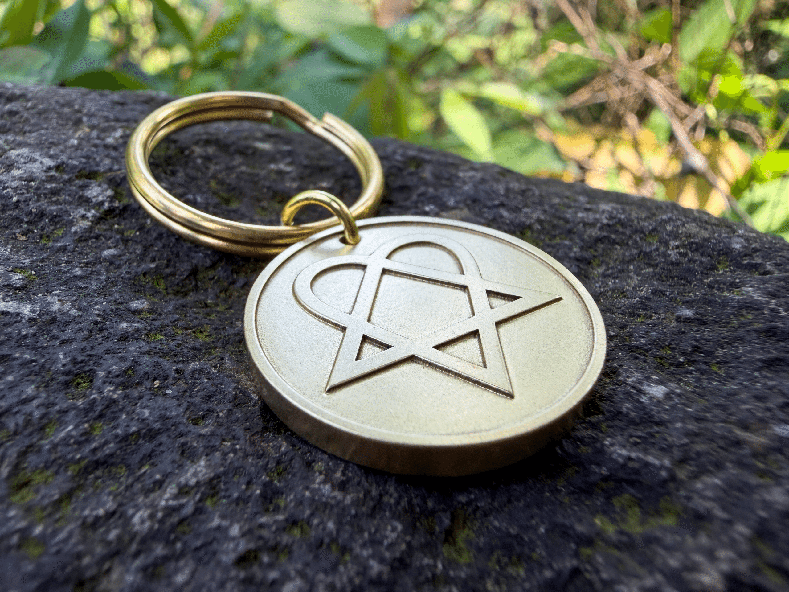 Brass keychain with an engraved heartagram symbol resting on a stone surface
