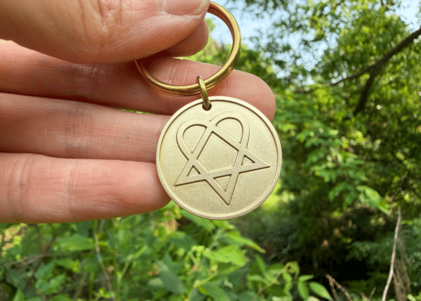 Hand holding a circular brass keychain engraved with a heartagram symbol