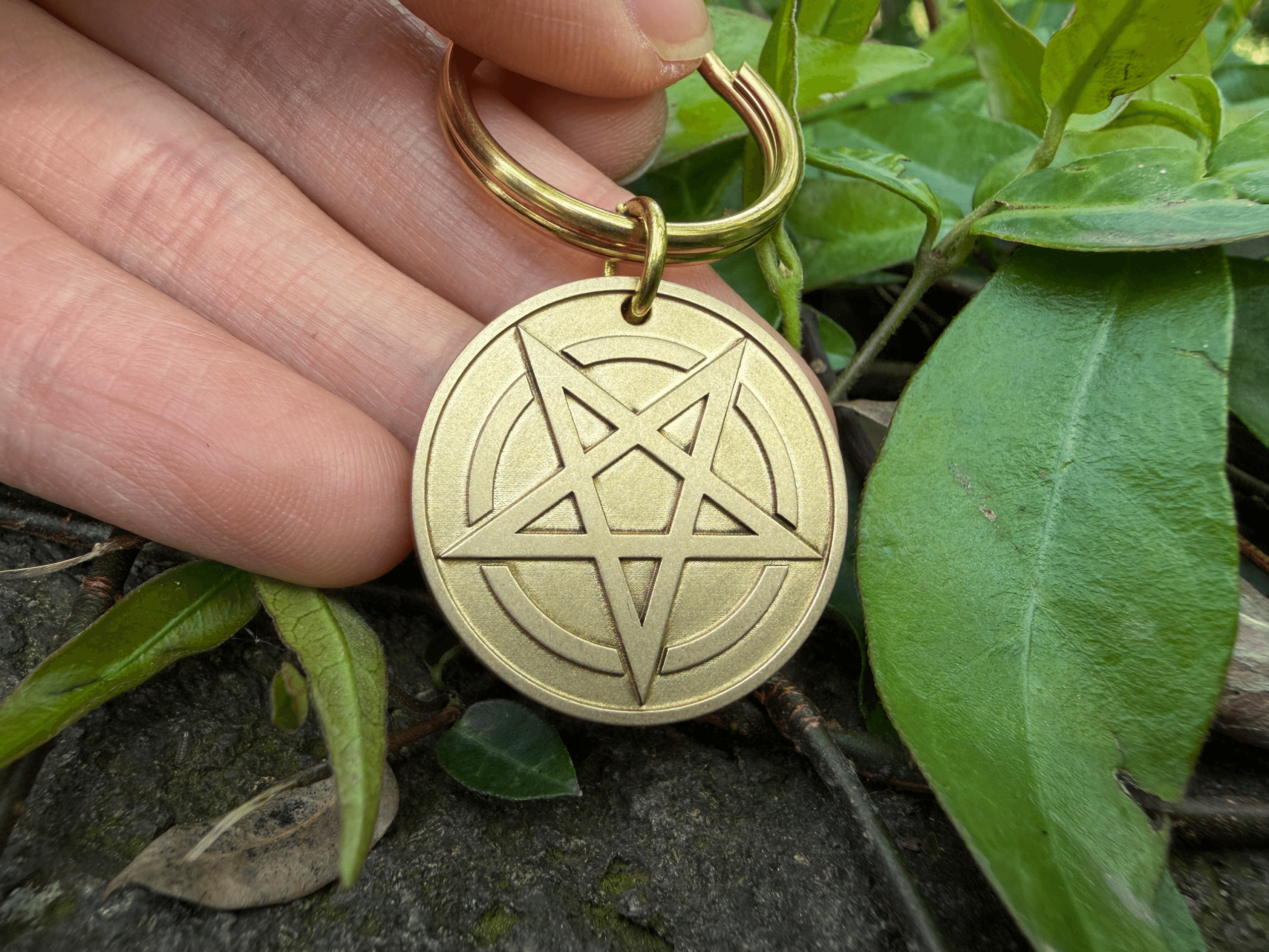 Hand holding a circular brass keychain featuring an engraved inverted pentagram design
