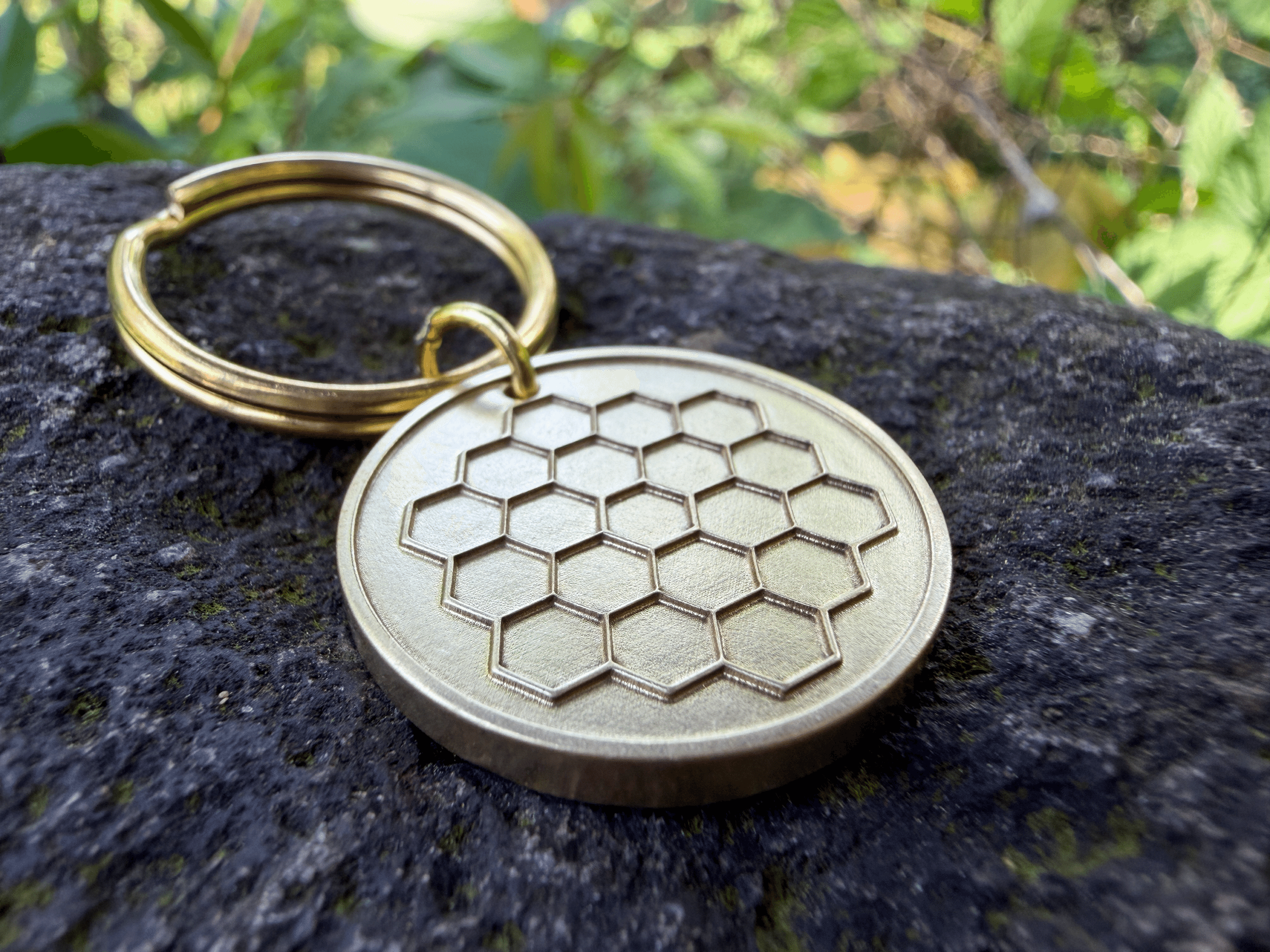 Brass circular keychain tag with an engraved James Webb Space Telescope pattern resting on a stone surface