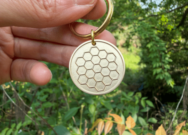 Hand holding a circular brass keychain tag with an embossed James Webb Space Telescope pattern