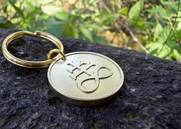 Brass keychain medallion featuring an embossed Leviathan cross symbol resting on a dark rock