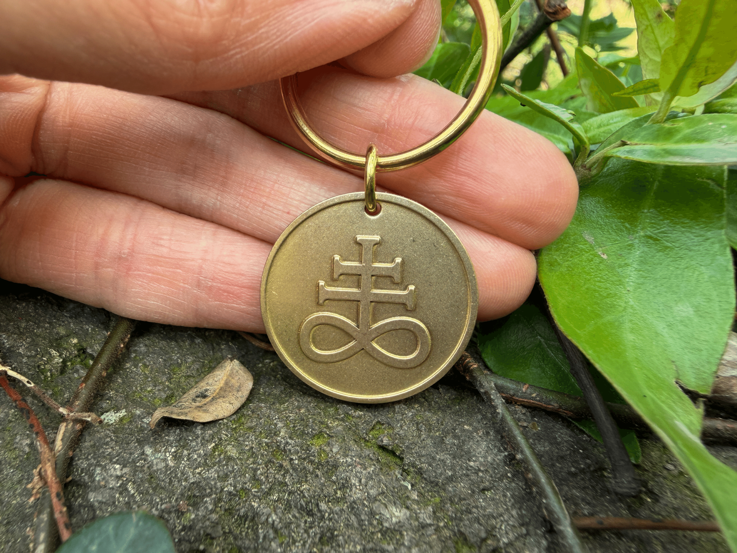 Hand holding a brass keychain with an engraved Leviathan cross symbol