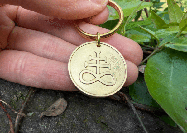 Hand holding a circular brass keychain engraved with a Leviathan cross symbol