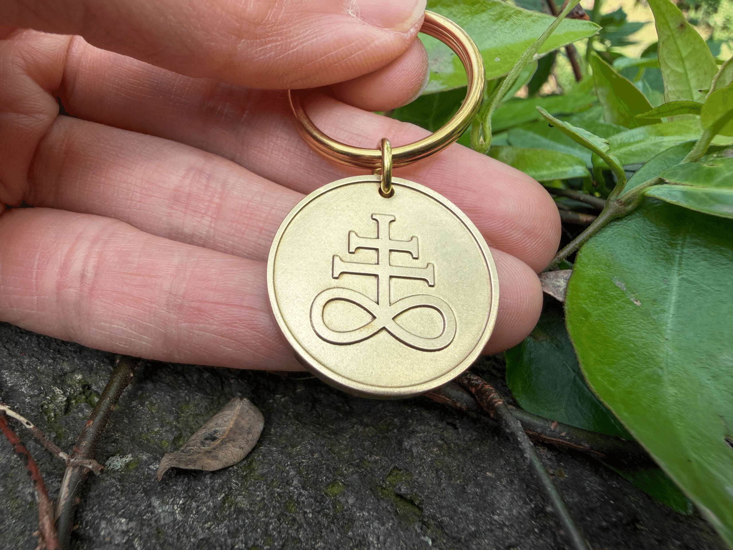 Hand holding a circular brass keychain engraved with a Leviathan cross symbol