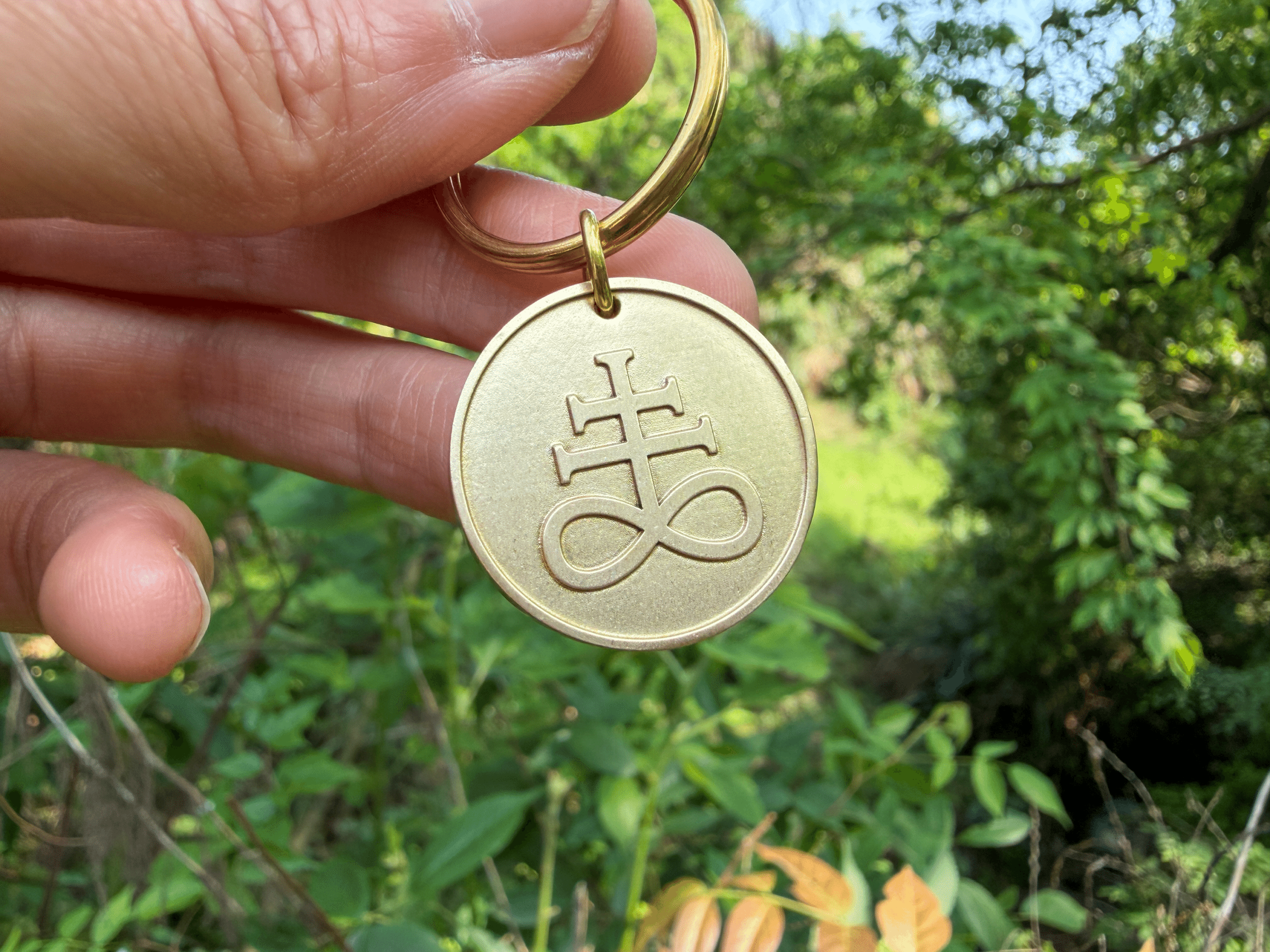 Hand holding a brass keychain tag engraved with a Leviathan cross symbol