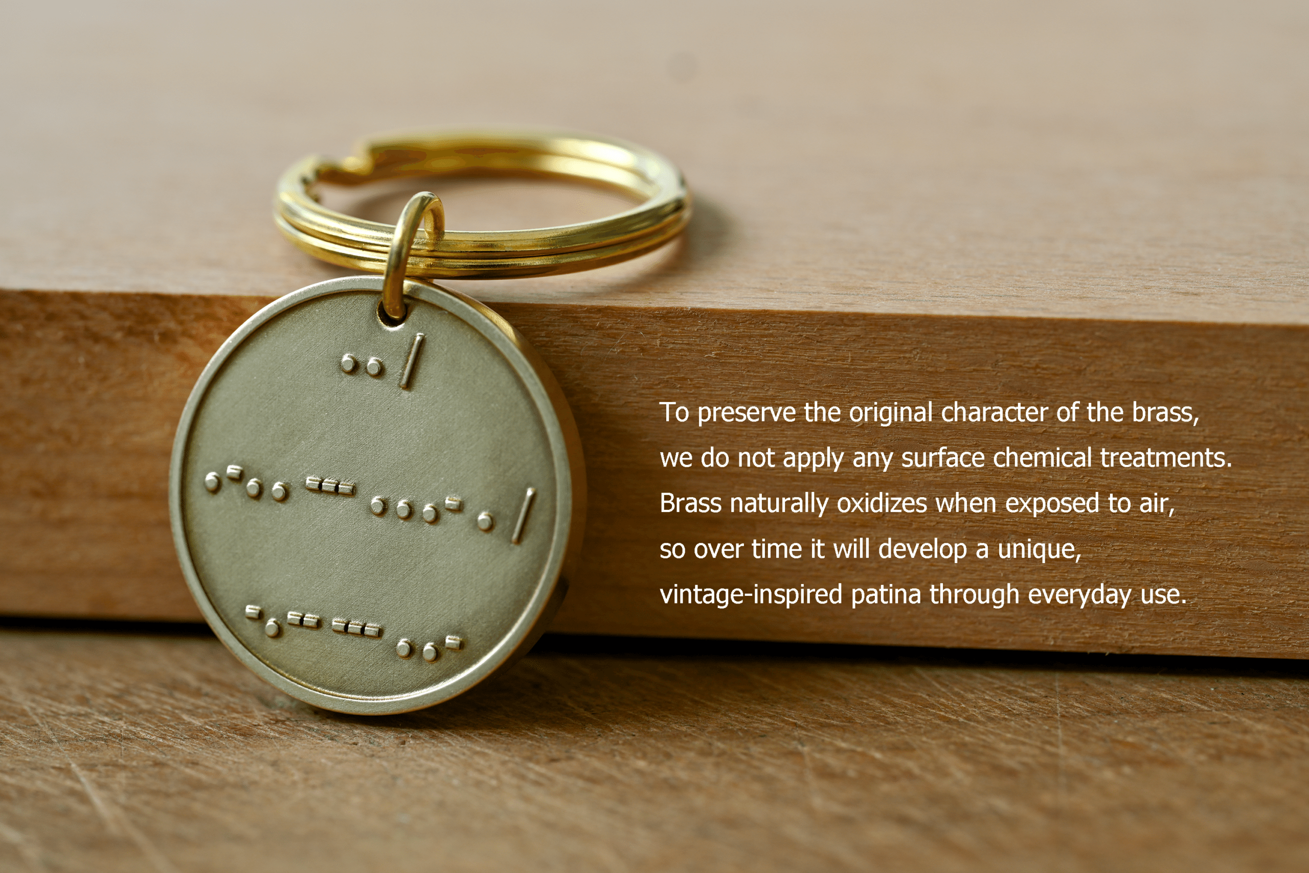 Round brass keychain tag with raised symbols alongside text explaining that untreated brass oxidizes over time to form a unique patina