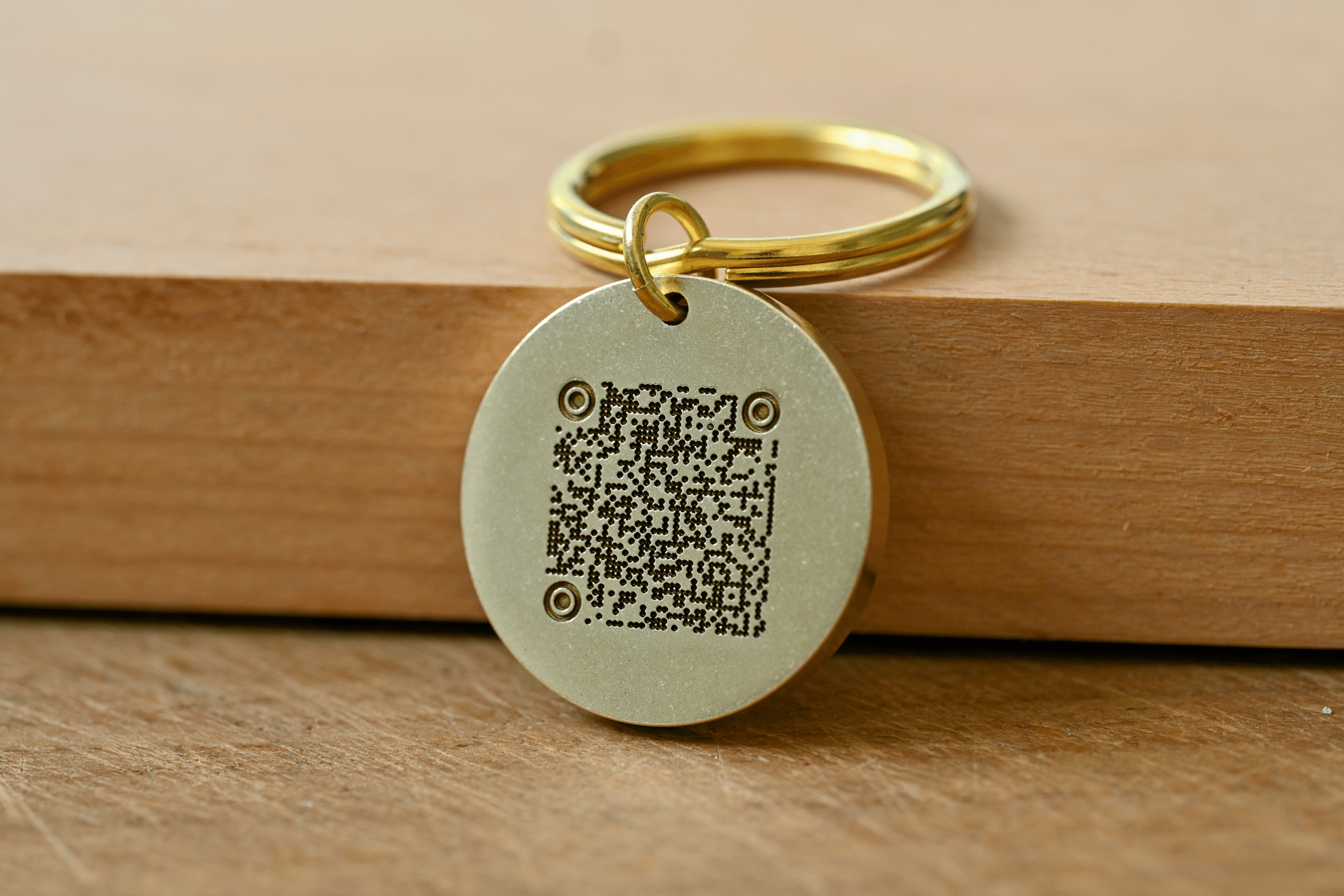 Round brass keychain tag with an engraved QR code resting on a wooden surface