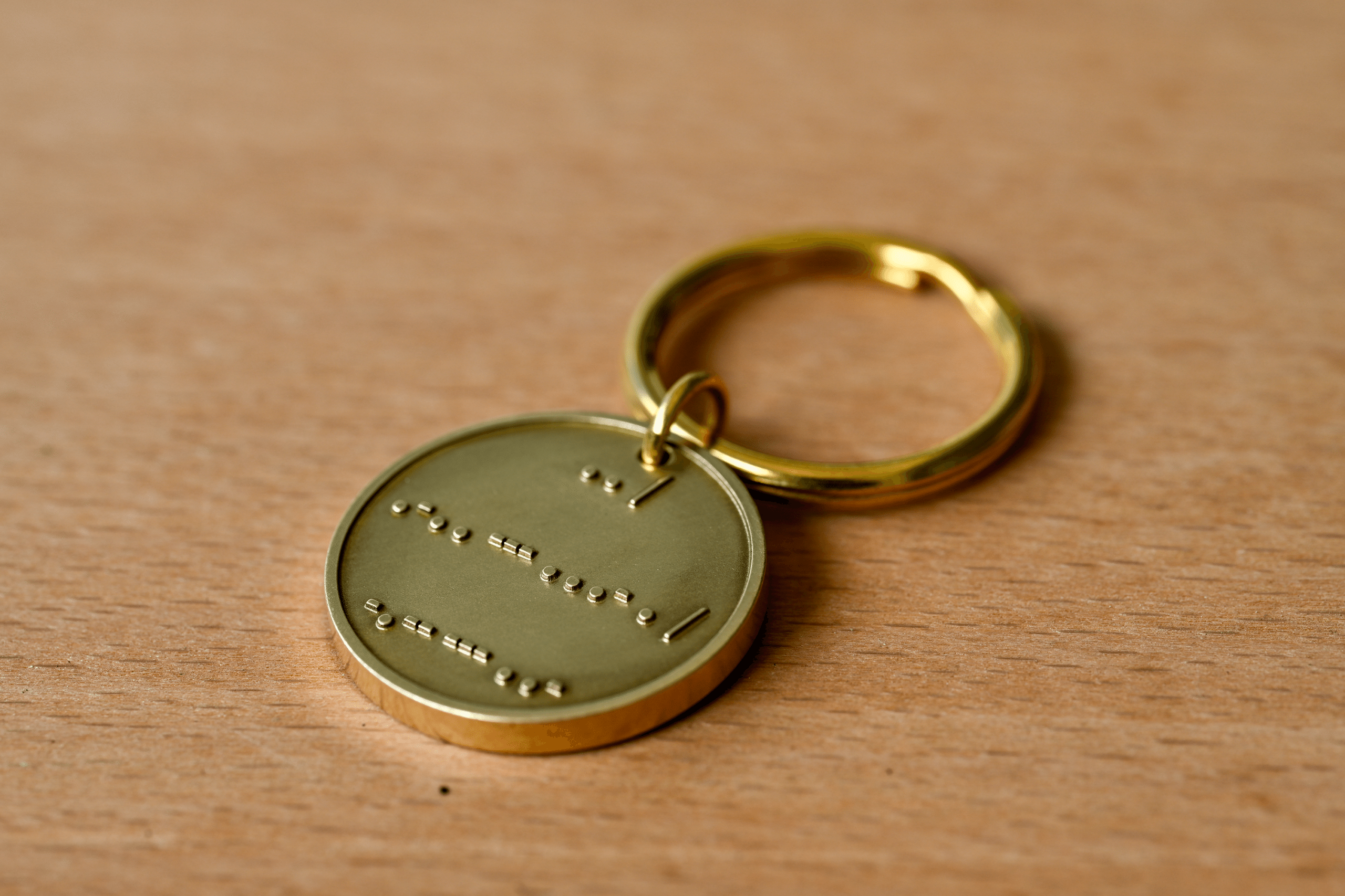 Brass keychain tag with raised Morse code dots and dashes on a wooden surface