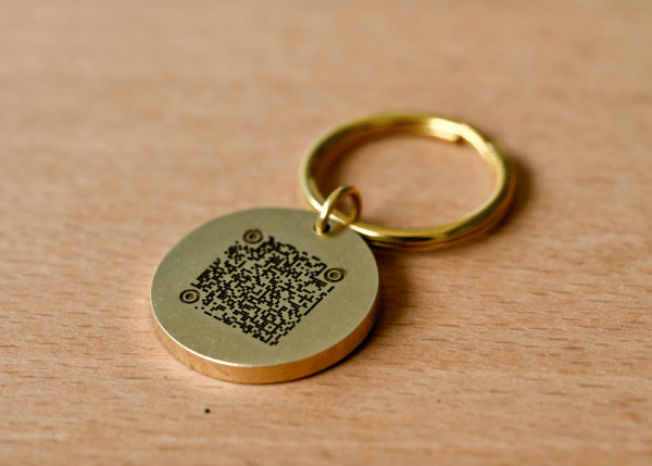 Round brass keychain tag with an engraved QR code resting on a wooden surface
