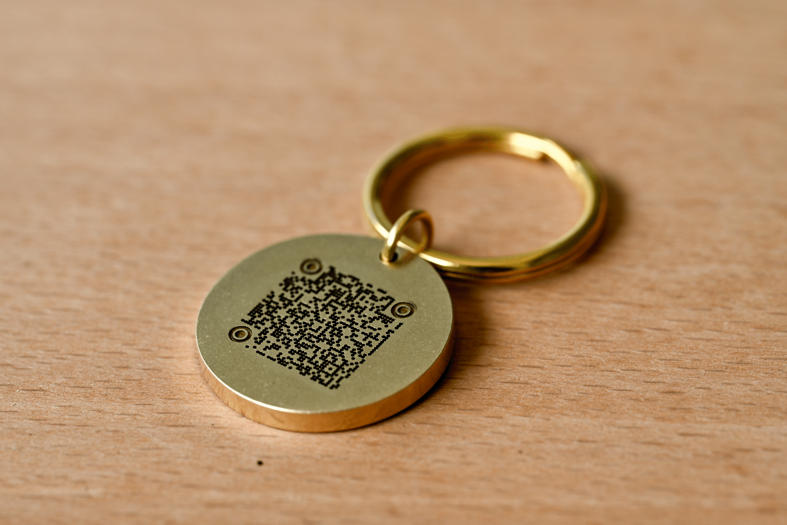 Round brass keychain tag with an engraved QR code resting on a wooden surface