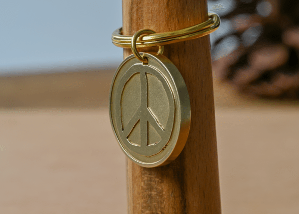 Brass peace sign keychain hanging on a wooden post