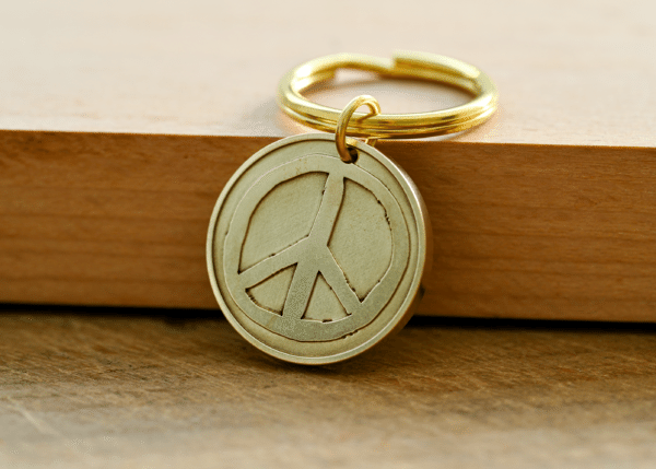 Brass keychain with a circular peace sign pendant resting on a wooden surface