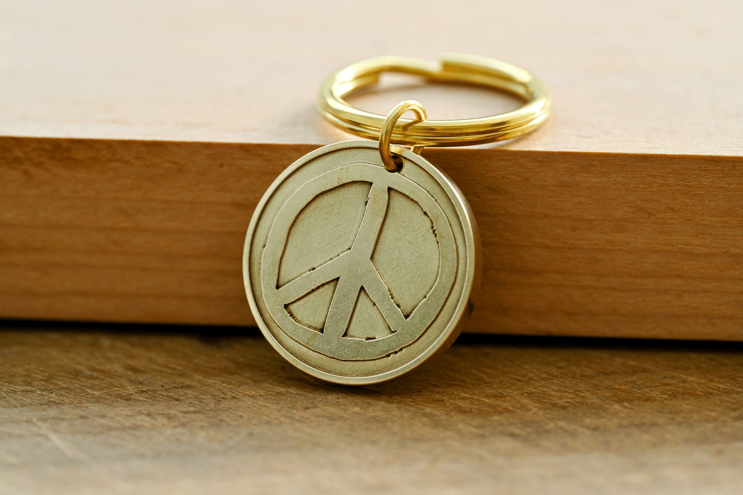 Brass keychain with a circular peace sign pendant resting on a wooden surface