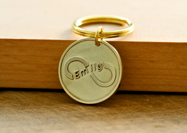 Round gold keychain tag engraved with an infinity symbol featuring the name Emily inside