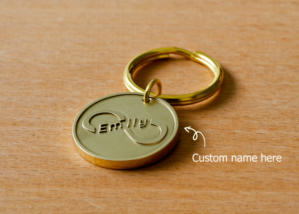 Round brass keychain featuring an infinity symbol engraved with the name Emily, with an arrow indicating Custom name here