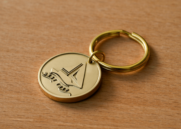 Gold keychain medallion featuring an engraved sailboat and the text BEST TRIP