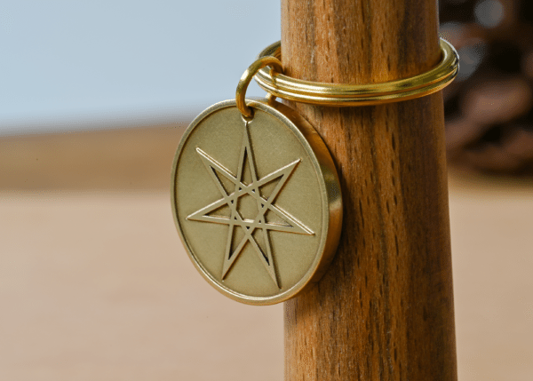 Brass circular keychain engraved with a seven-pointed star hanging on a wooden peg