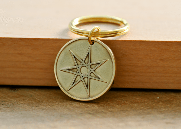 Brass key ring with a circular pendant featuring an engraved seven-pointed star resting on a wooden surface
