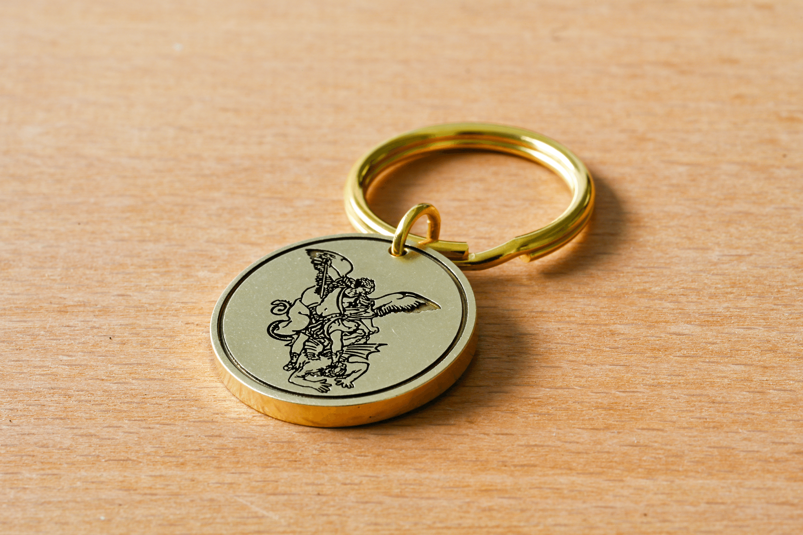 Gold metal keychain with a circular pendant engraved with Saint Michael the Archangel defeating a demon
