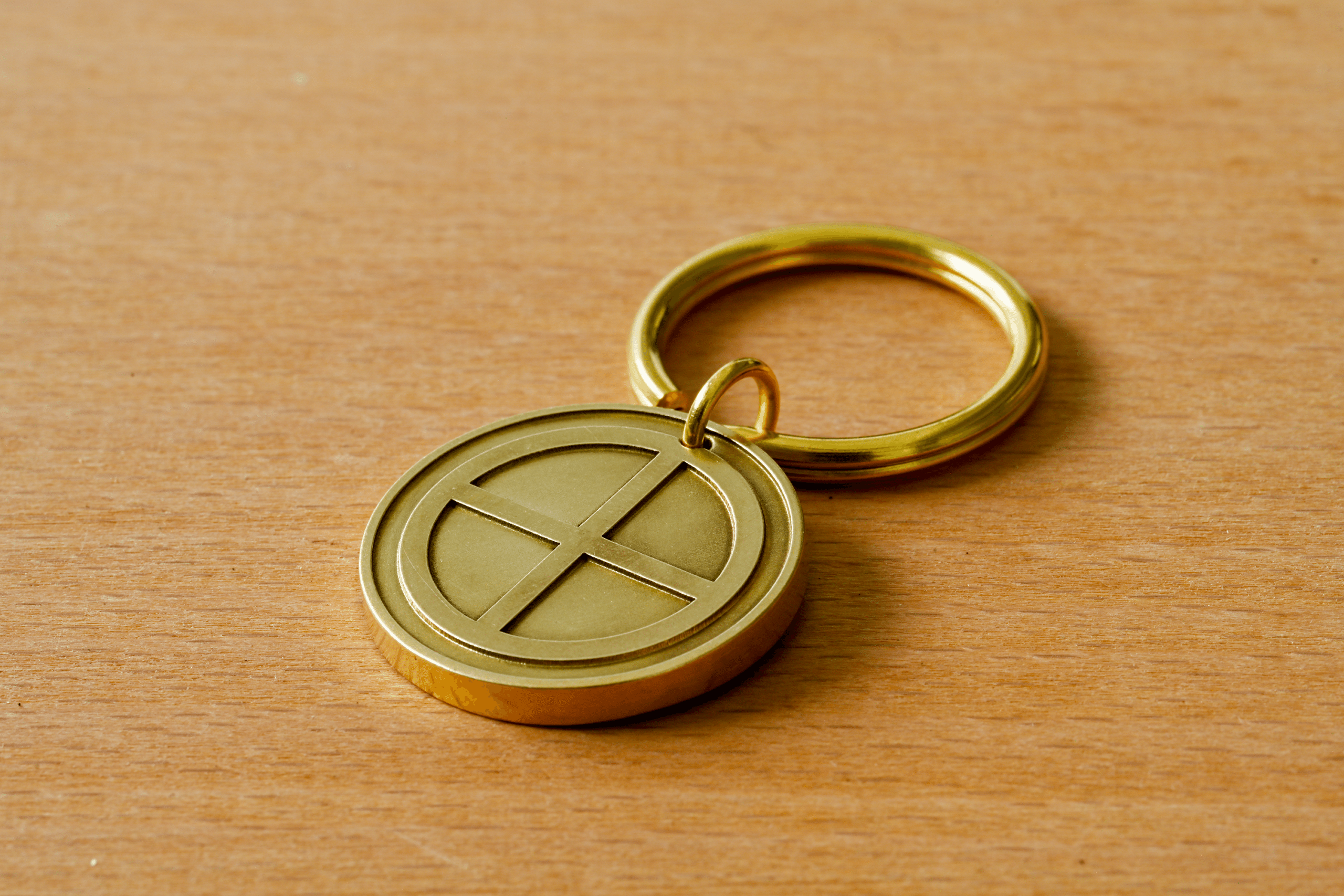 Gold-colored metal keychain with a circular sun cross medallion resting on a wooden surface