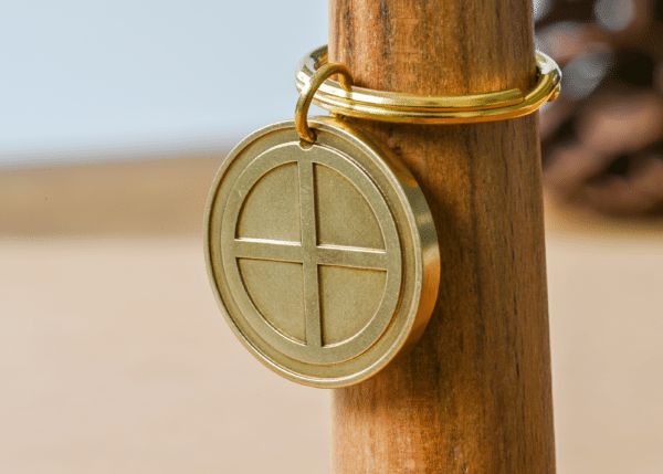 Round brass keychain tag engraved with a solar cross symbol attached to a gold key ring