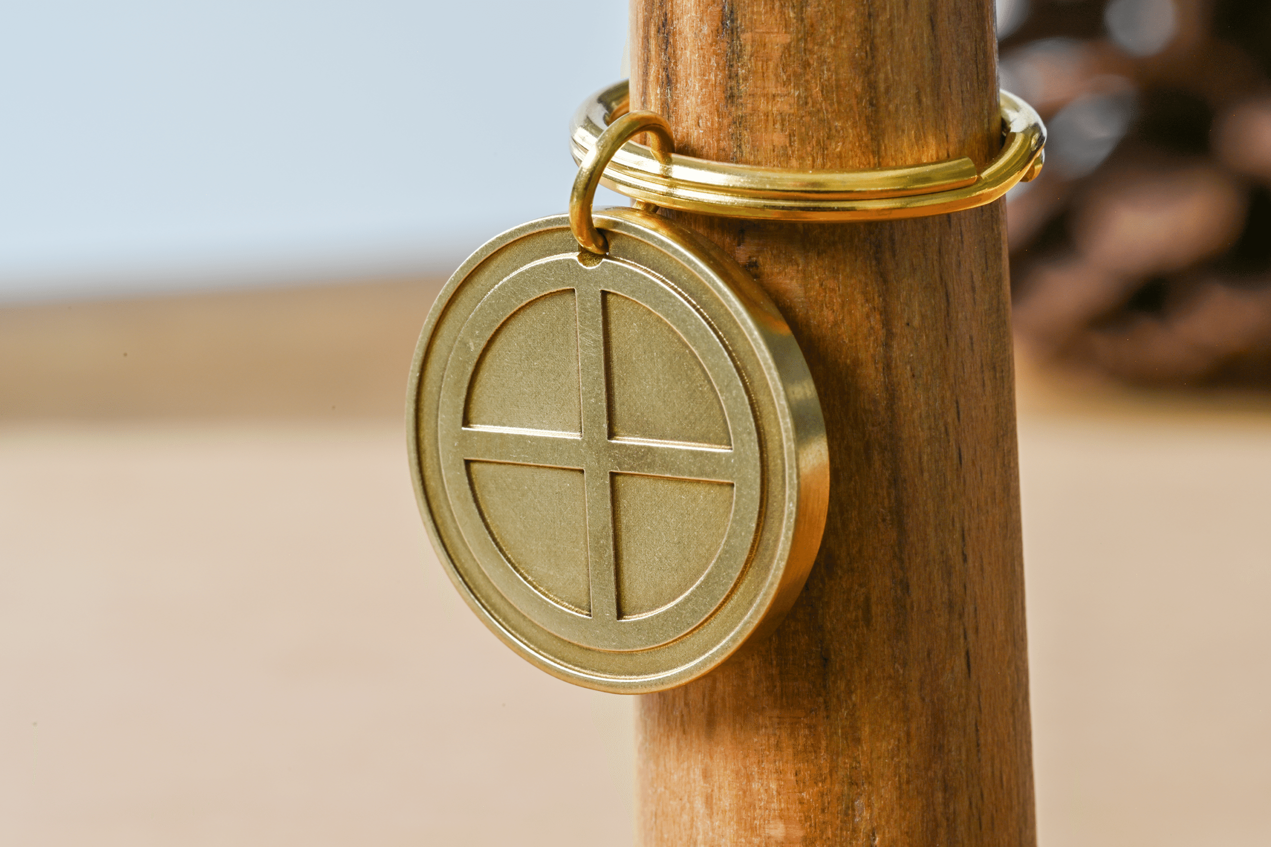 Round brass keychain tag engraved with a solar cross symbol attached to a gold key ring