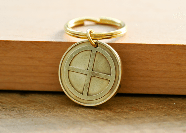 Brass sun cross key ring featuring a circular pendant engraved with a cross design, resting on a wooden surface