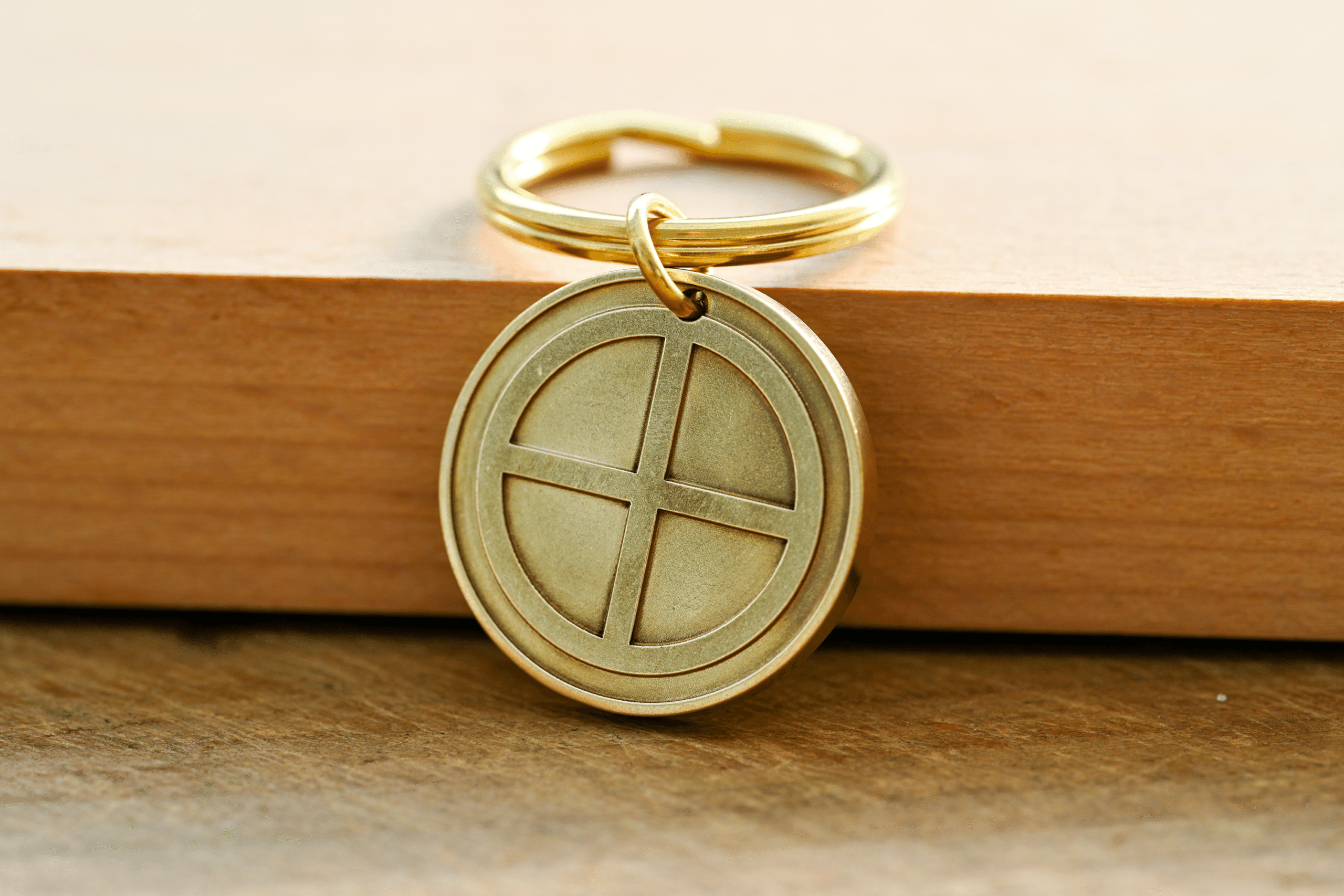 Brass sun cross key ring featuring a circular pendant engraved with a cross design, resting on a wooden surface