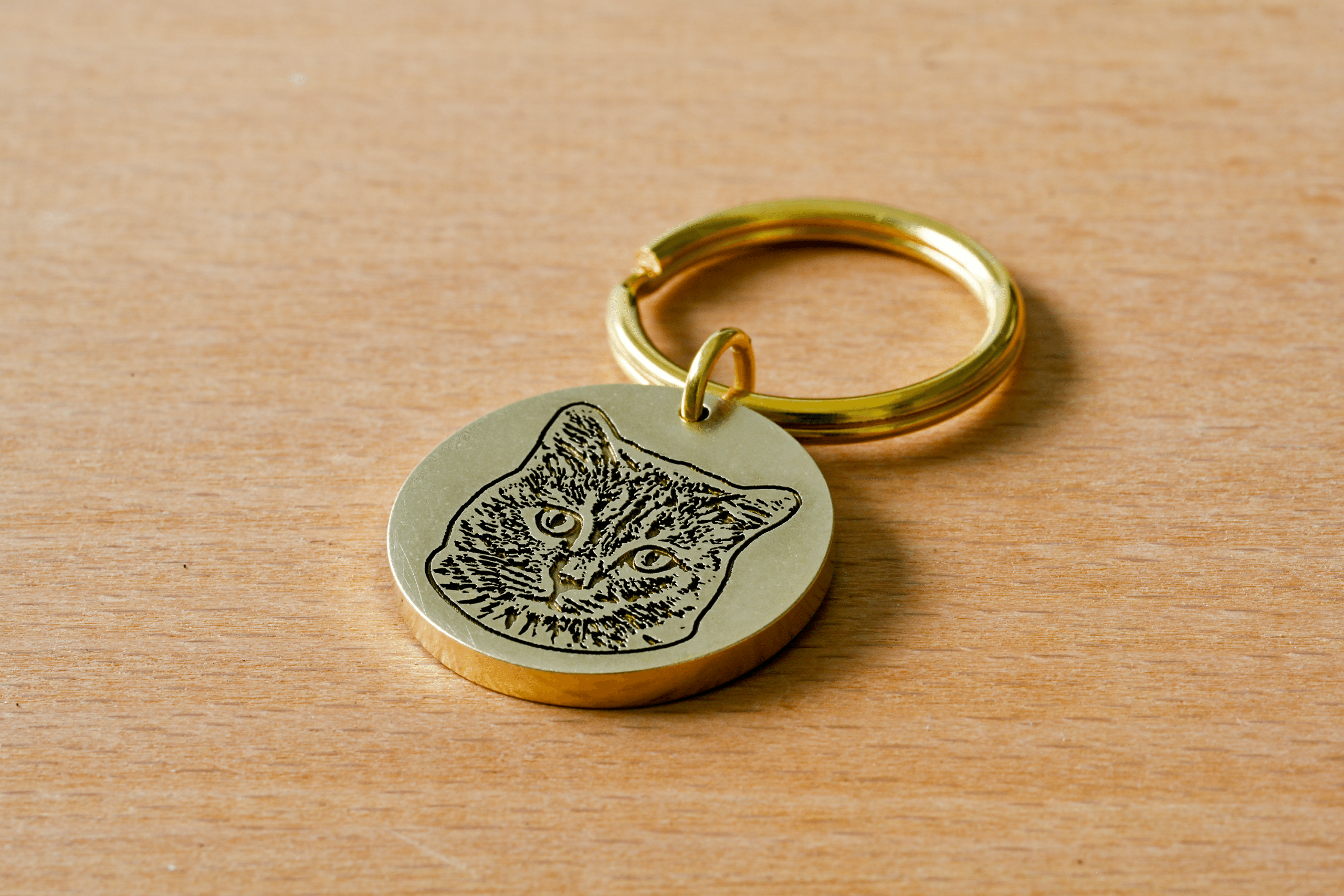 Round brass keychain tag engraved with a detailed portrait of a cat's face