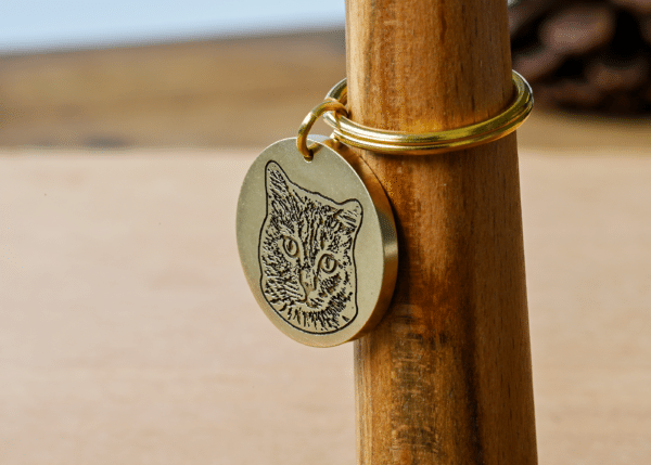Round brass tag engraved with a detailed portrait of a cat face attached to a keyring