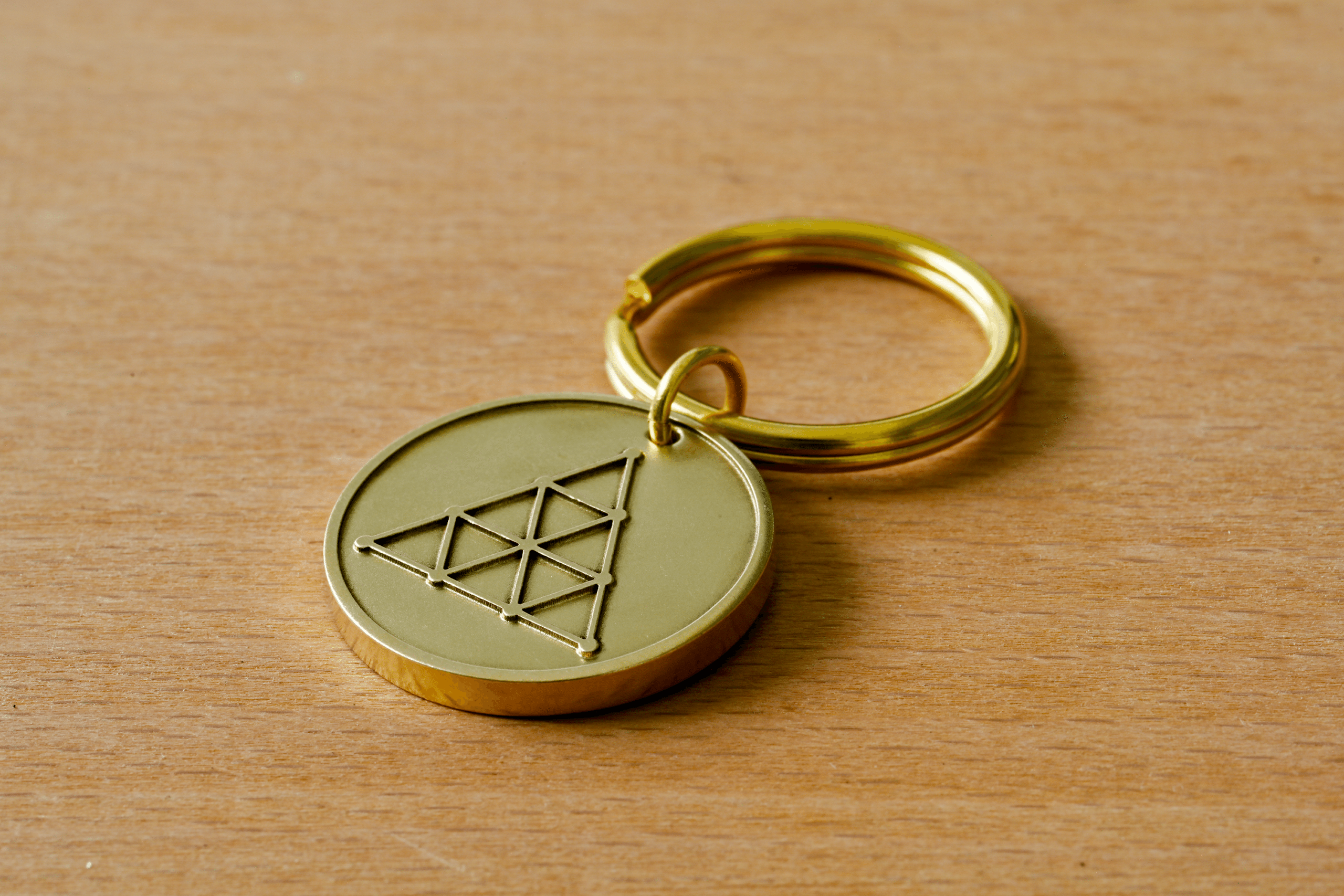 Gold brass keychain with a circular medallion featuring a geometric triangle symbol on a wooden surface