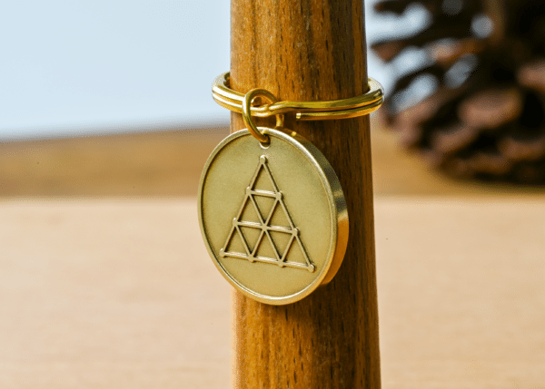 Brass circular keychain medallion engraved with a geometric triangle pattern