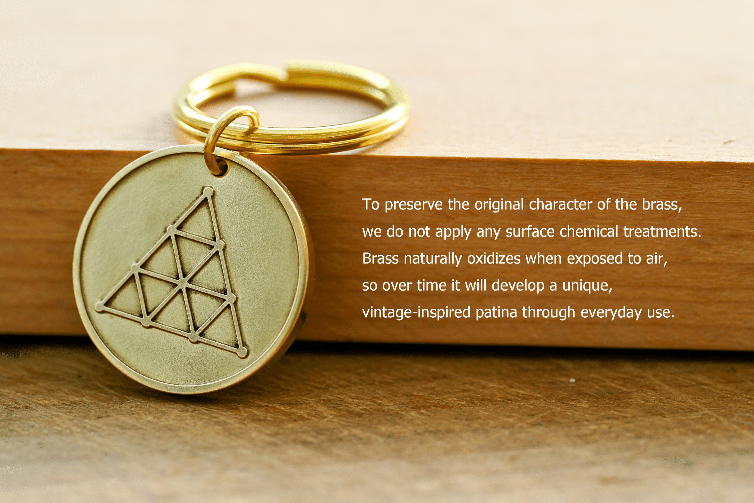 Brass keychain with a geometric triangle symbol alongside text: To preserve the original character of the brass, we do not apply any surface chemical treatments. Brass naturally oxidizes when exposed to air, so over time it will develop a unique, vintage-inspired patina through everyday use
