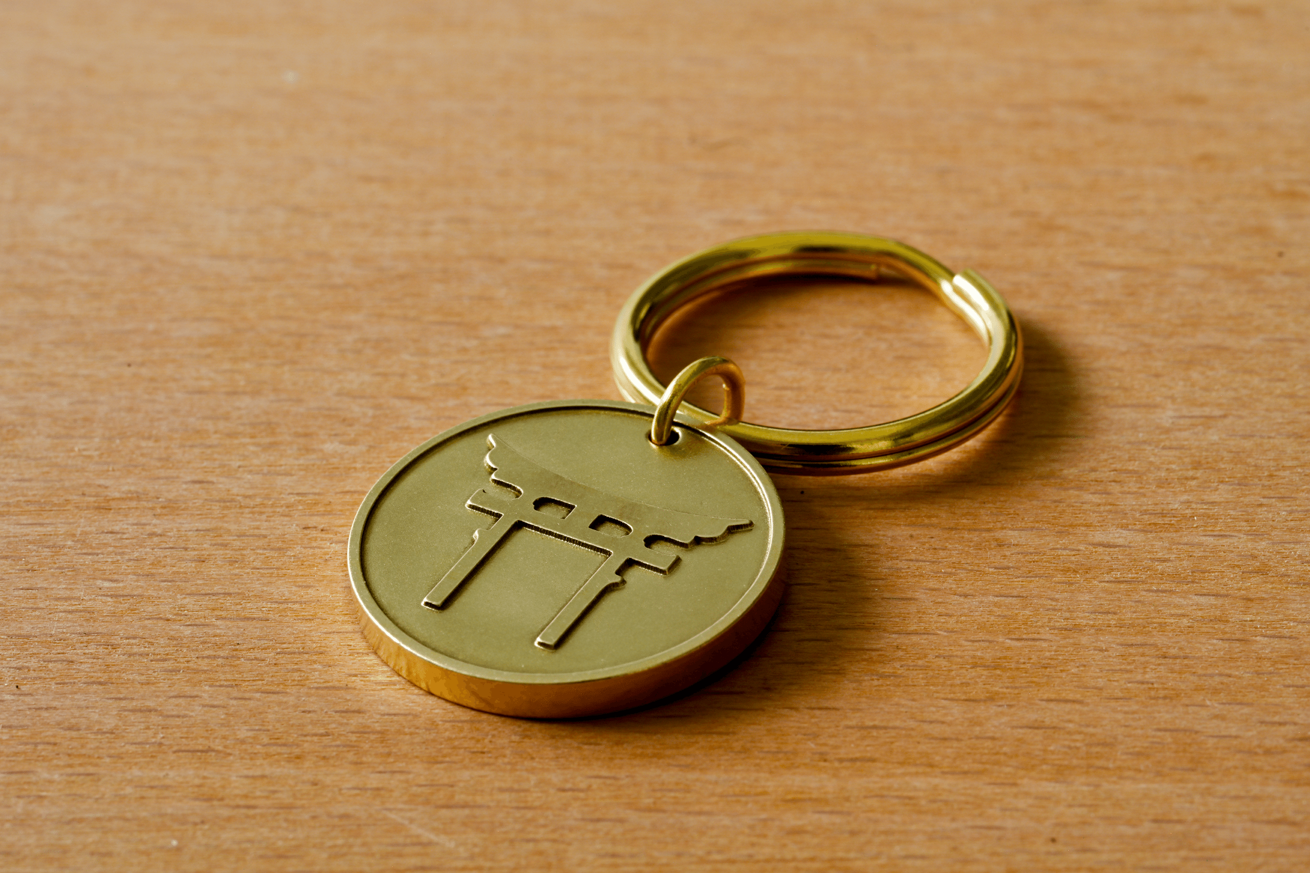 Gold circular keychain with an engraved torii gate on a wooden surface